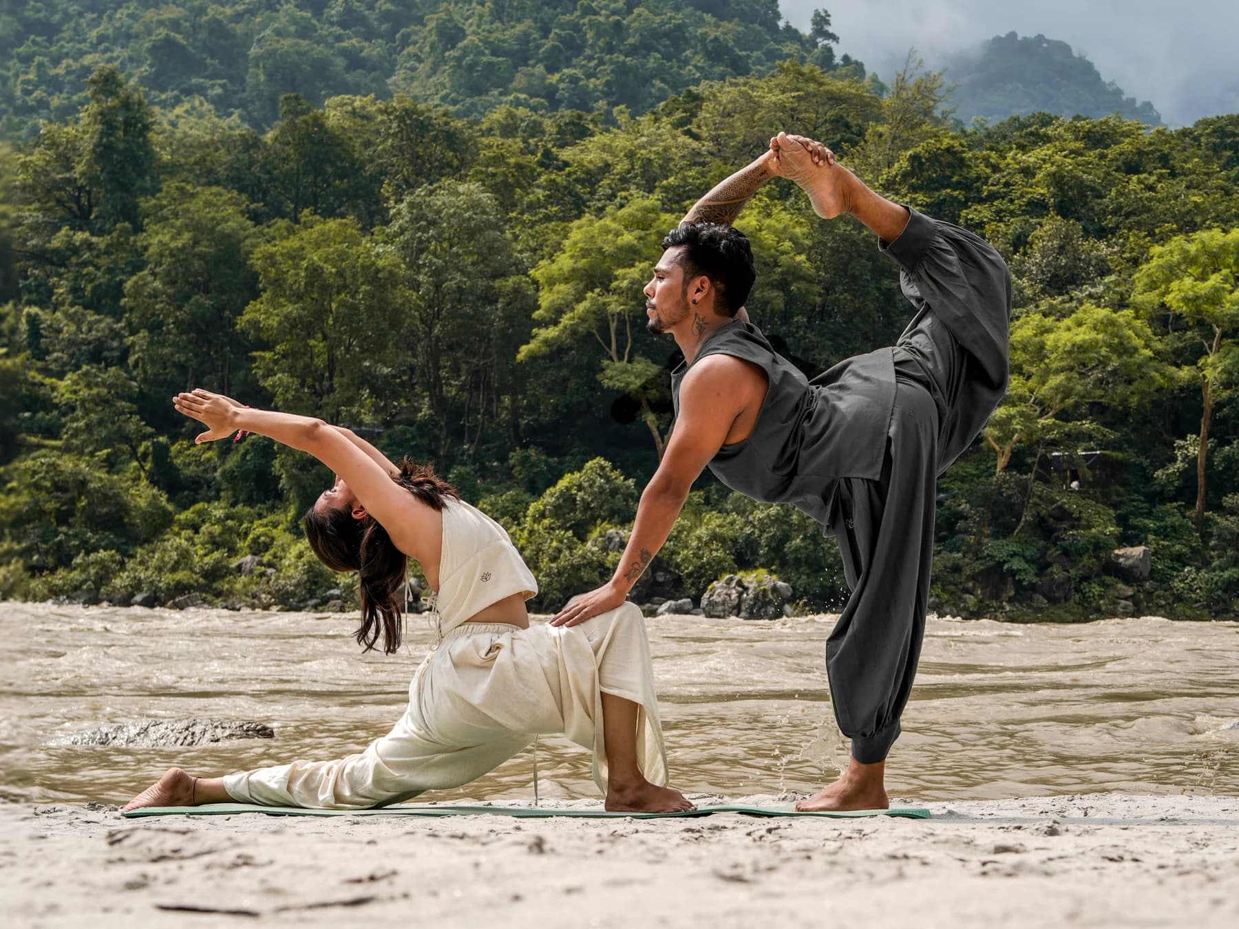 Two people practising yoga on a riverbank in Akiso yoga wear